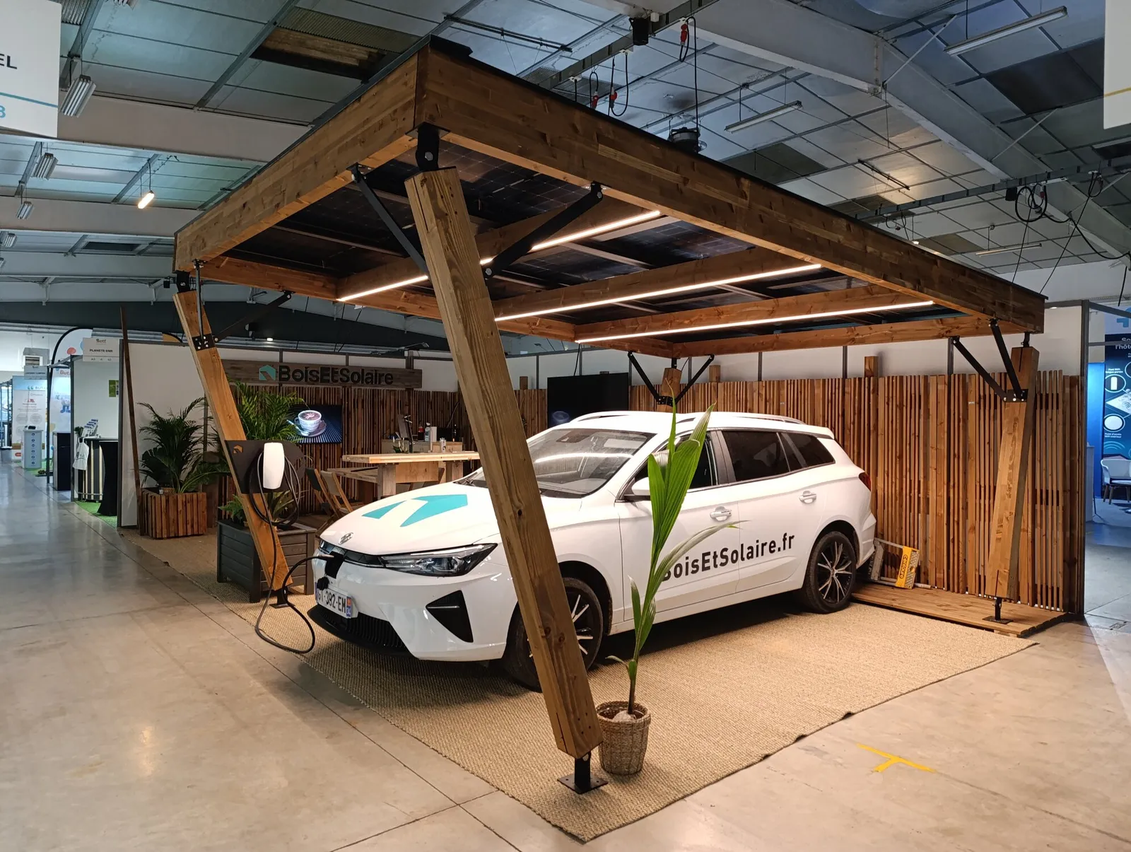 Une voiture électrique branchée à sa borne, sous un carport solaire en bois